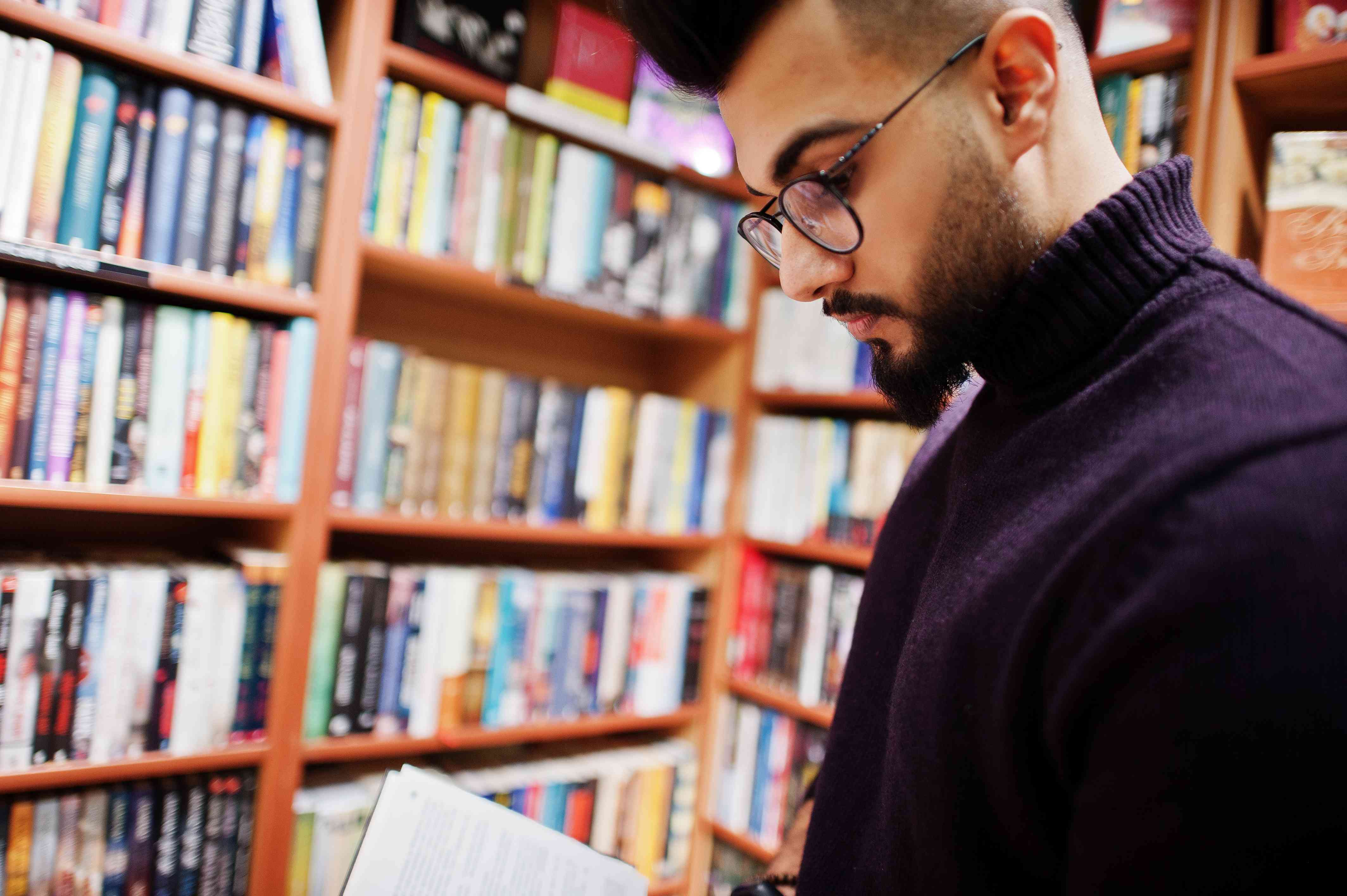 Foto Arabischer Student steht vor Regalen in einer Bibliothek und liest