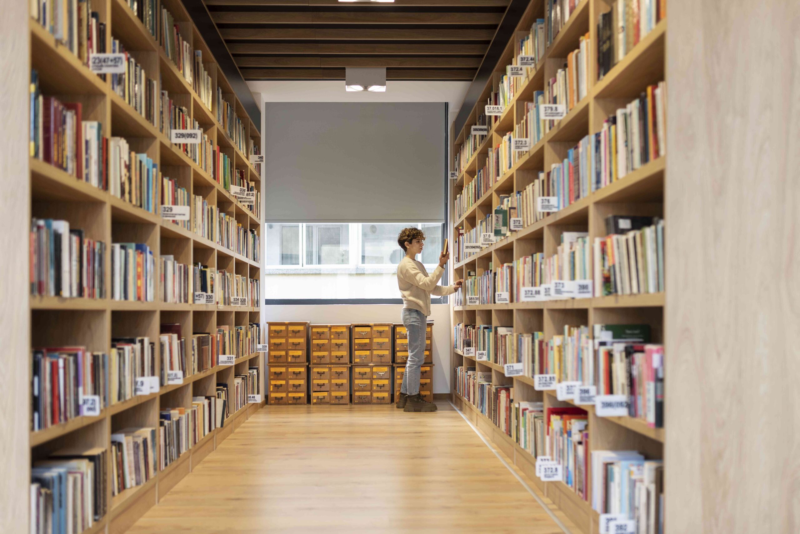 Foto einer Studetin, die zwischen den Regalen einer Bibliothek nach Büchern sucht