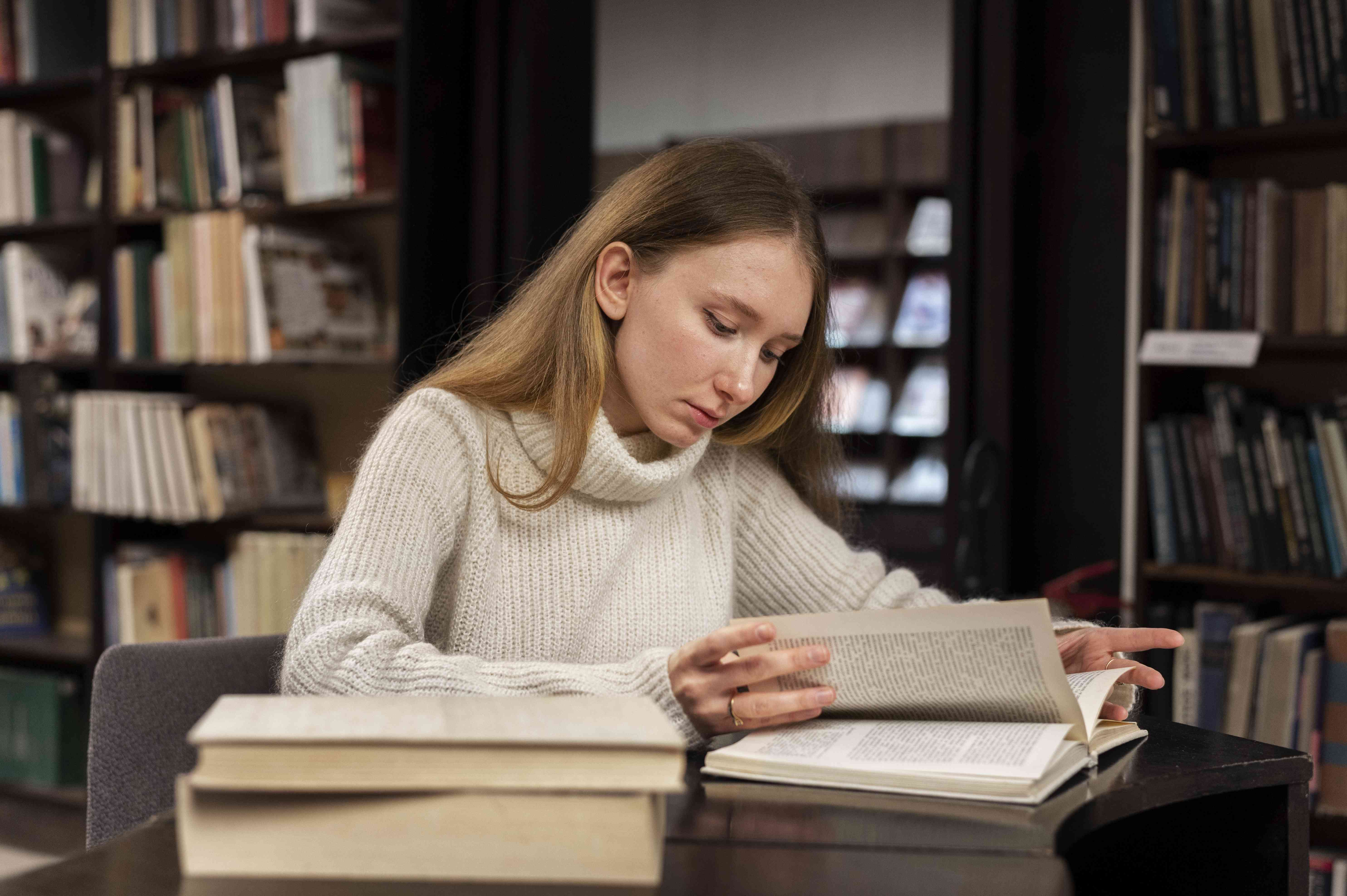 Foto einer Studentin in einer ehrwürdigen Bibliothek am Schreibtisch liest konzentriert in einem der Bücher vor ihr.